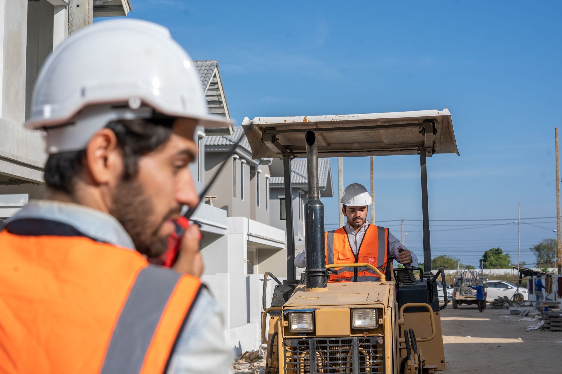 Construction workers wearing safety vests and helmets operating a vehicle at a building site.